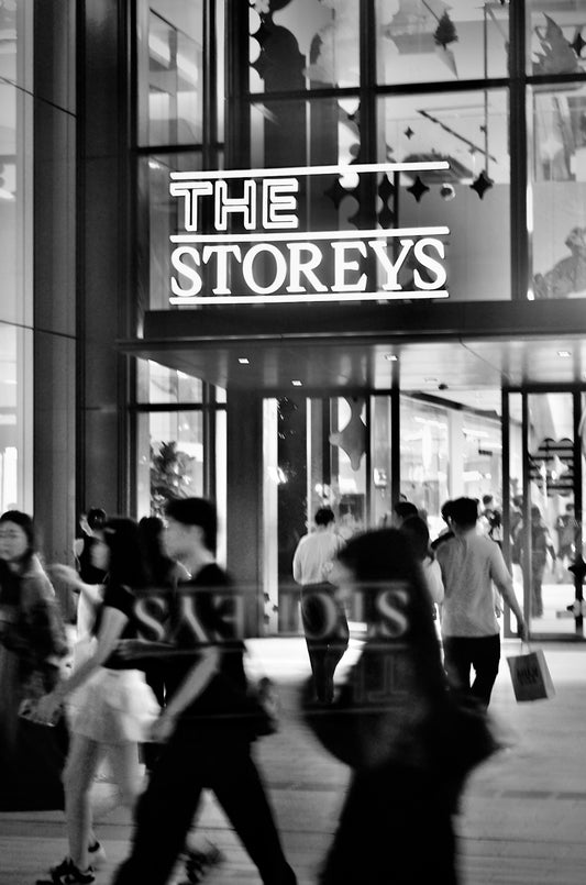A black and white photo of people walking in front of a store